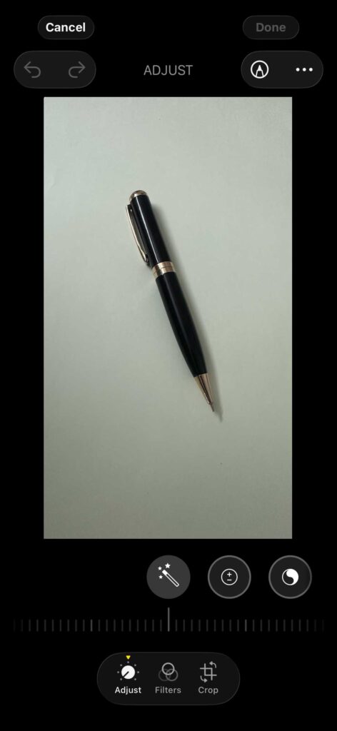 iPhone Photos app showing the Adjust editing tools with a pen placed on a light background